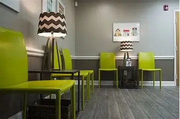 A waiting room with lime green chairs, two tables with black and white chevron lamps, gray walls, framed pictures, and wood-look flooring. The room has a modern, clean, and welcoming appearance.
