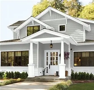 A modern two-story house with gray siding, white trim, a covered front porch with columns, multiple windows, a glass front door, and neatly landscaped shrubs in front.